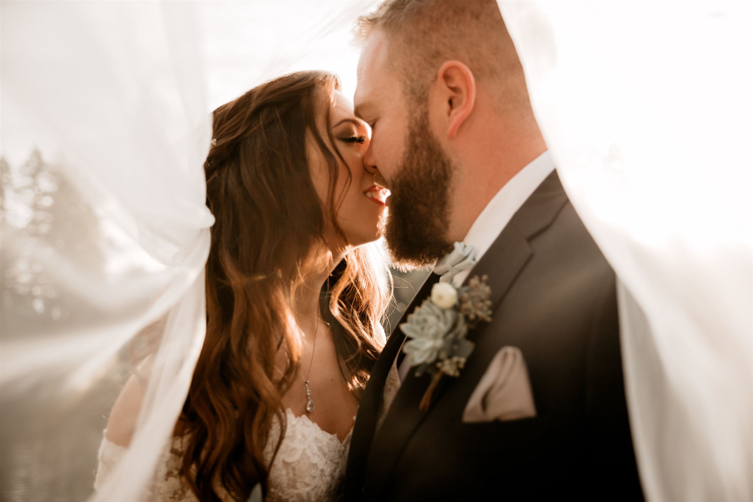 Bride and groom under veil sharing a kiss