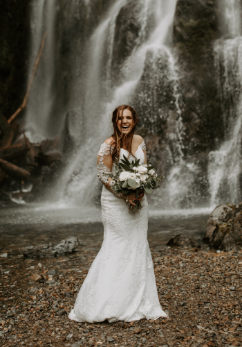 bride in wedding dress holding floral bouquet by waterfall