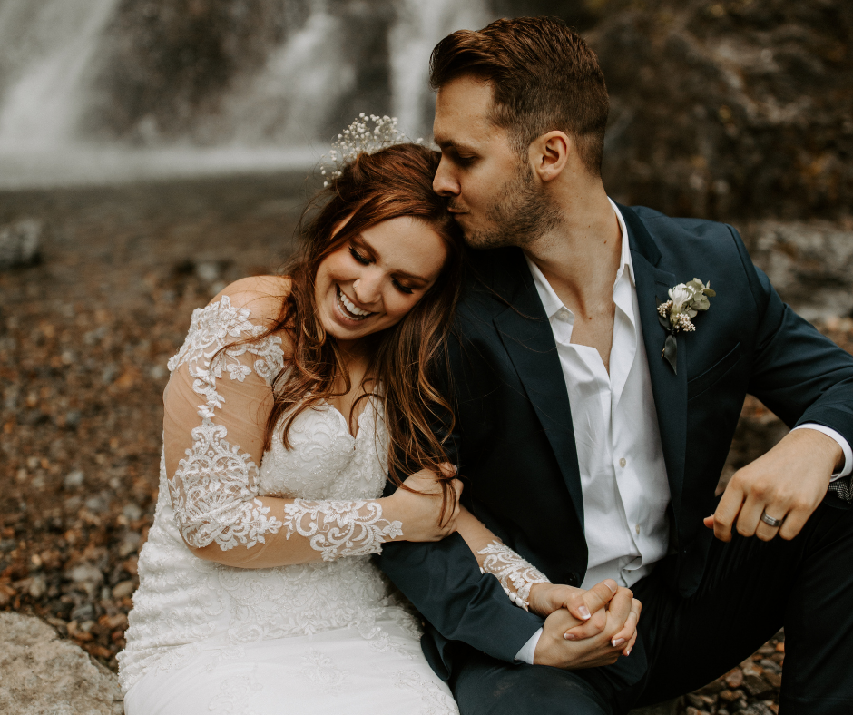groom kissing bride on the forehead by waterfall