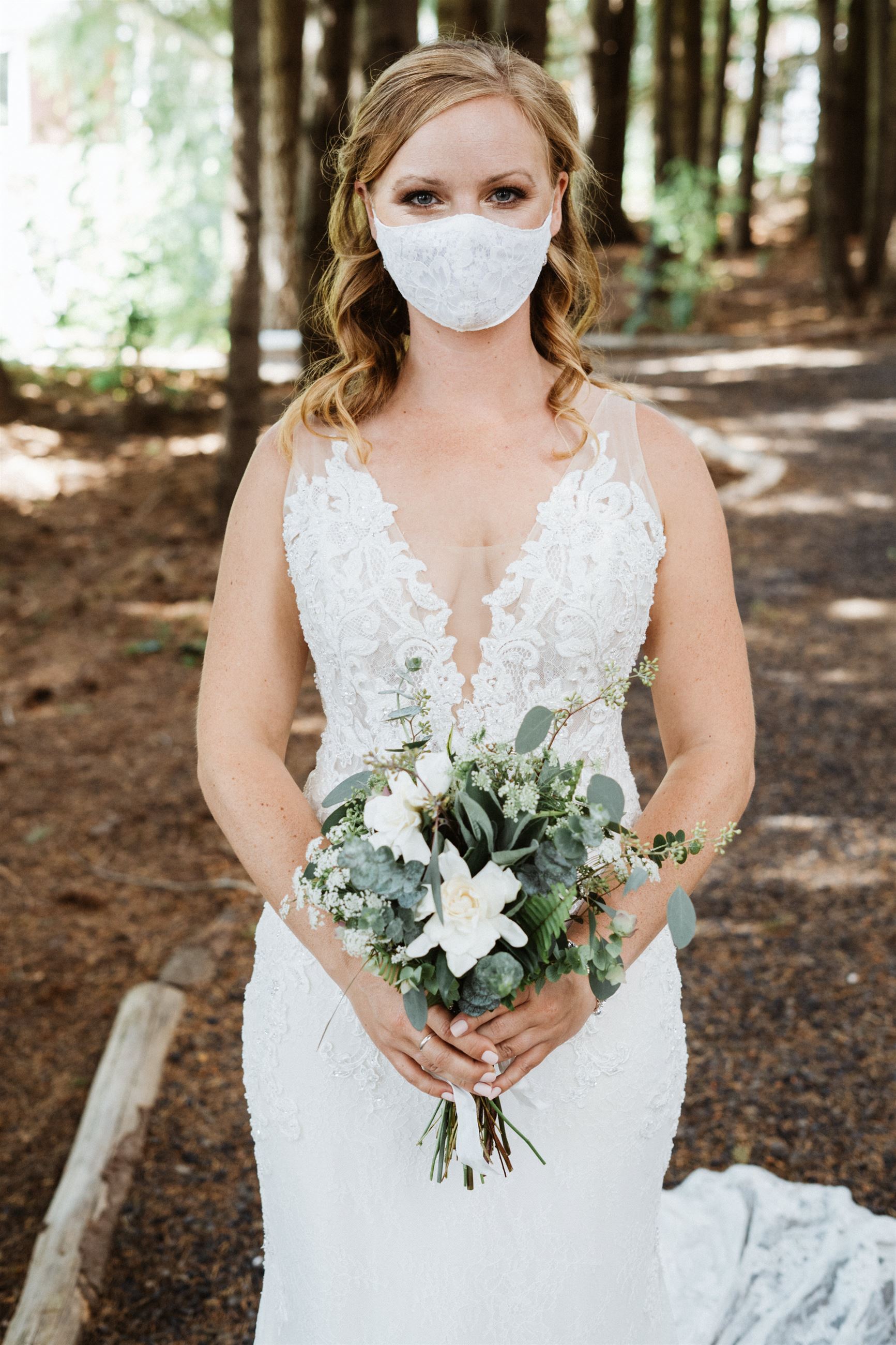 bride holding bouquet wearing lace wedding dress in mask