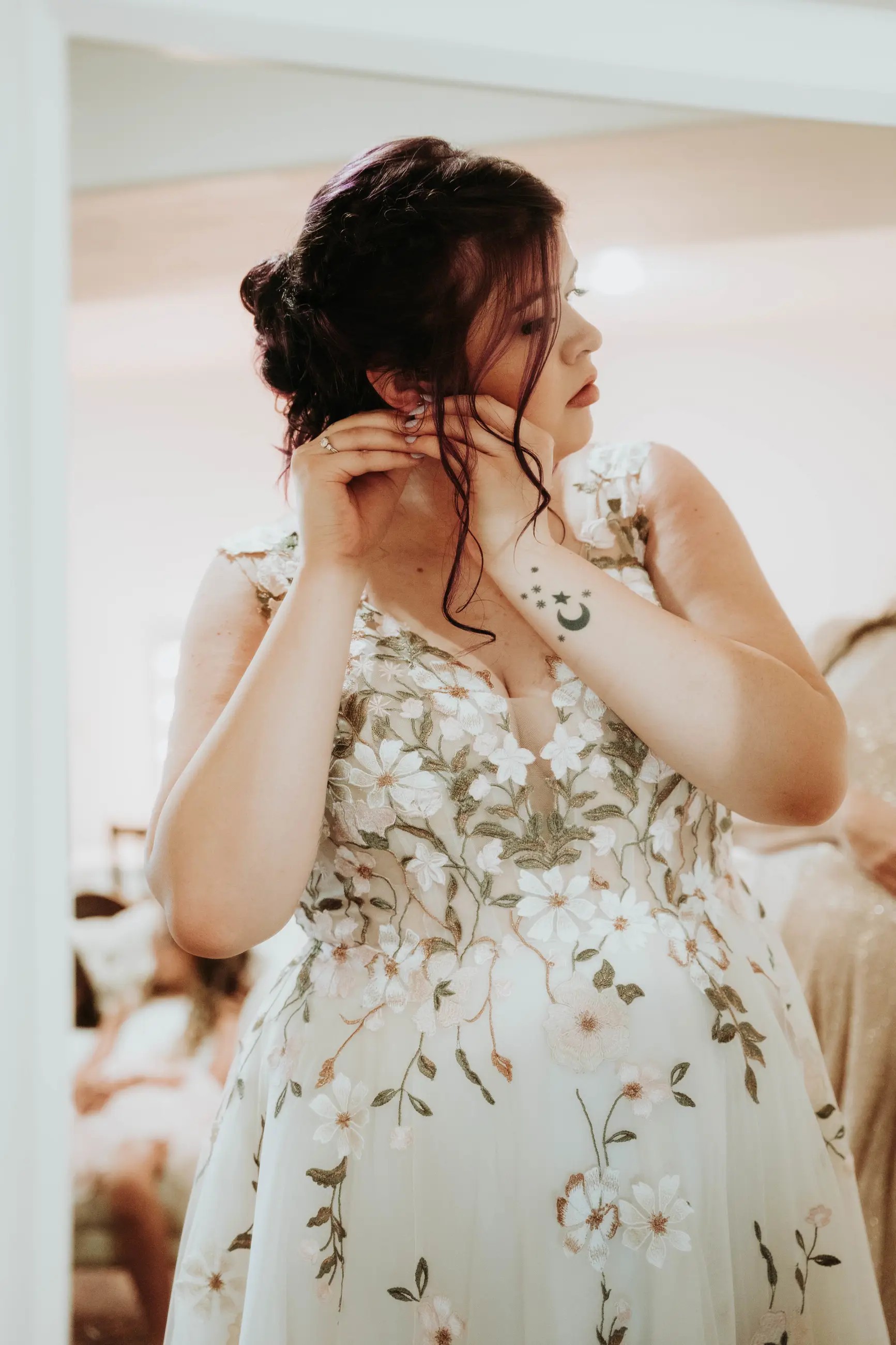 Bride putting on earrings, floral wedding dress